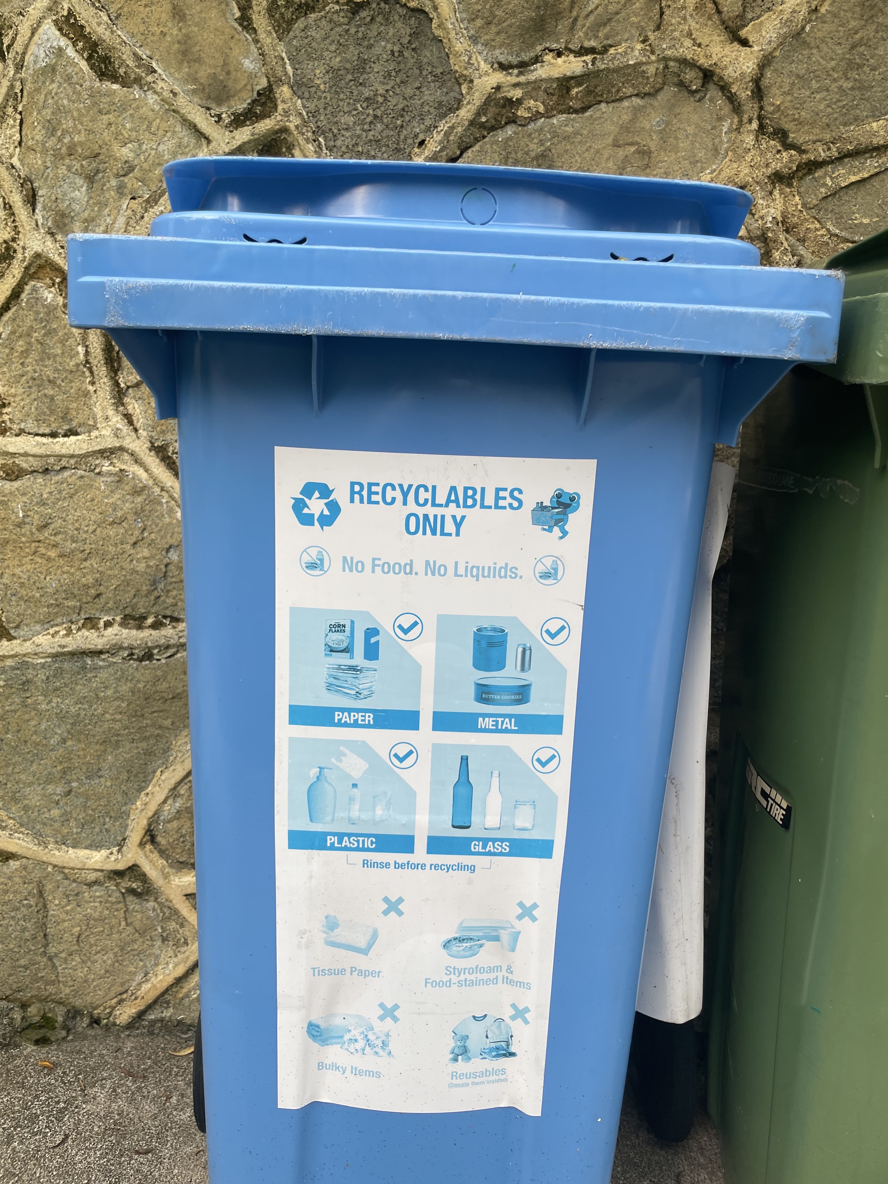 A blue recycling bin with instructions for paper, metal, plastic, and glass